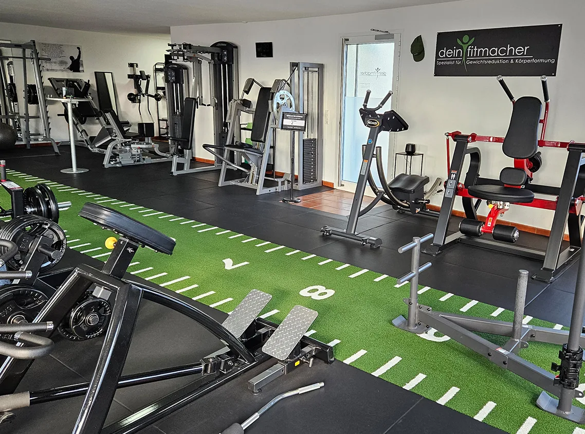 Leeres Personal Training Studio mit Trainingsgeräten und grüner Kunstrasenfläche