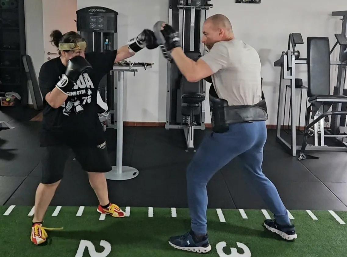 Frau beim Boxtraining mit einem Trainer und Schlagpolstern
